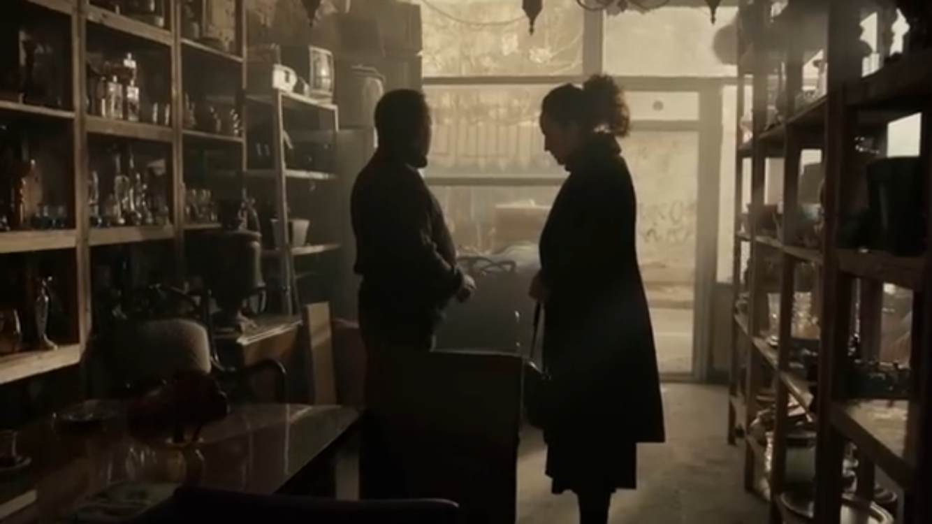 Bir Deli Sevda — Two figures silhouetted in a shop filled with warm window light.