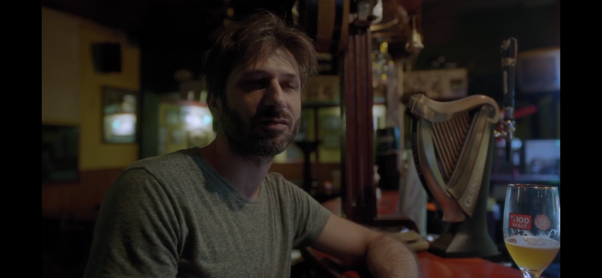 Diyalog — A man seated beside a glass at a bar.