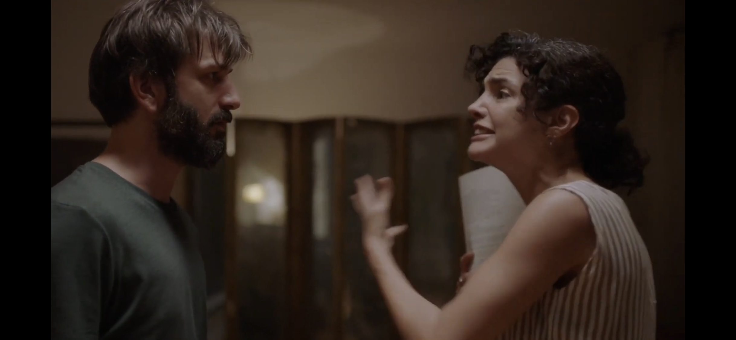 Diyalog — A woman raising her hand while speaking to a man indoors.