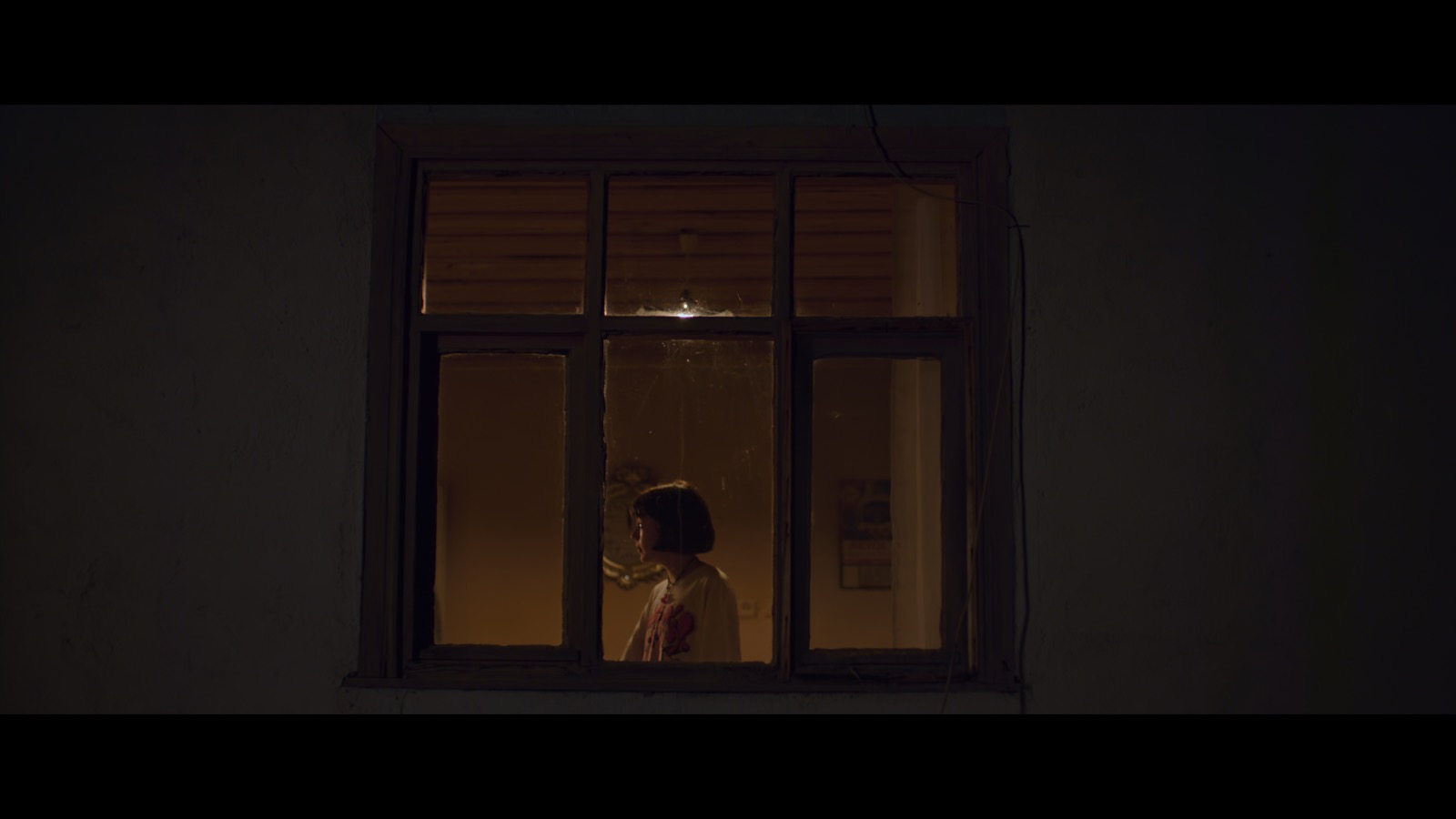 Kabahat — A girl seen through a warmly lit window at night.