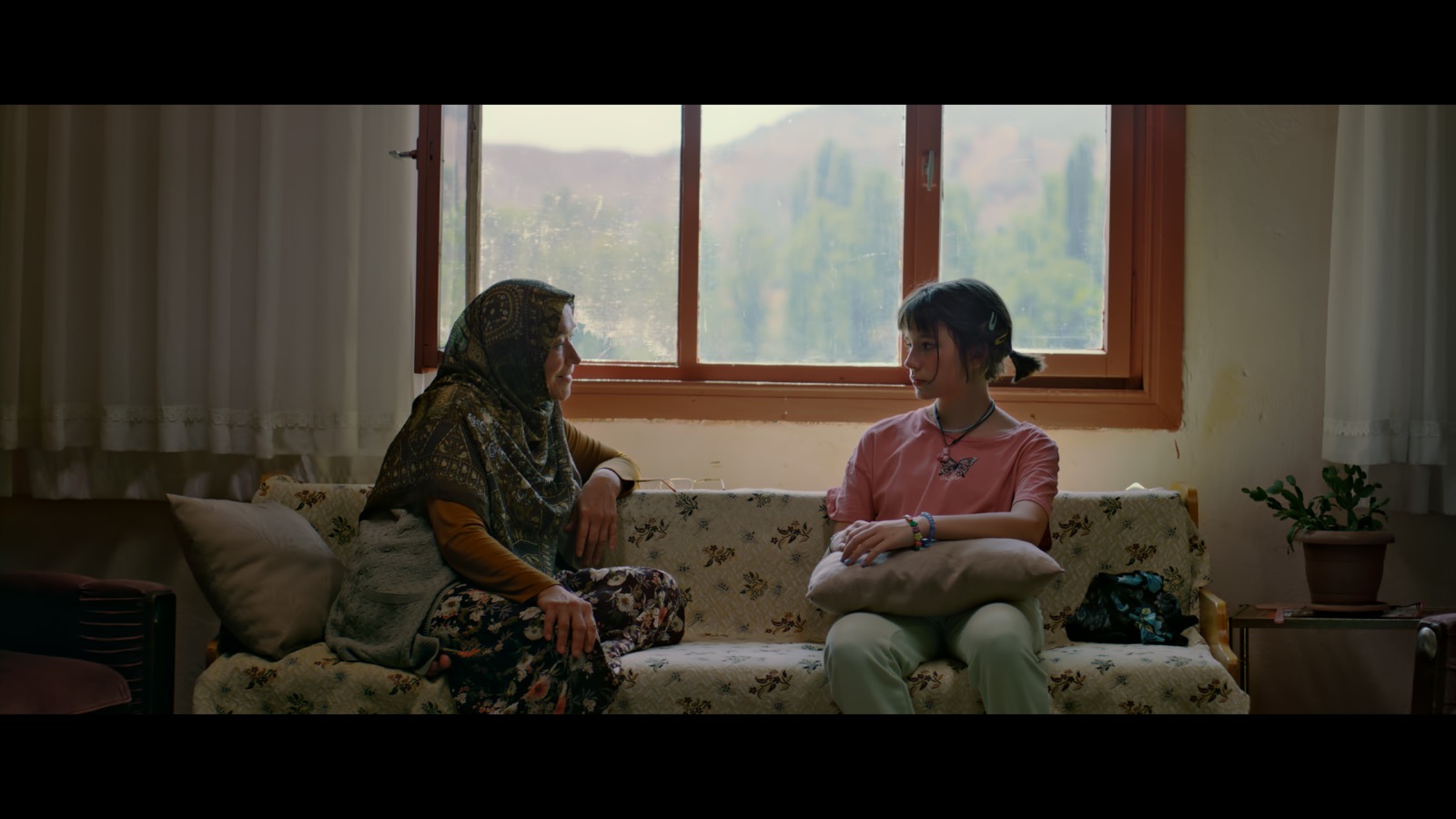 Kabahat — A woman and a girl seated together below a window.