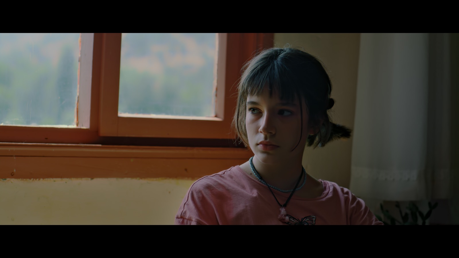 Kabahat — A girl in a pink shirt beside a sunlit wooden window.