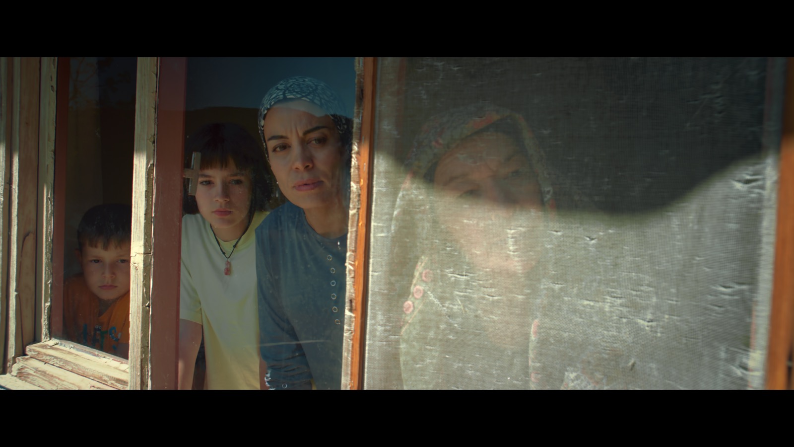 Kabahat — Two children and two women looking out through a wooden window.