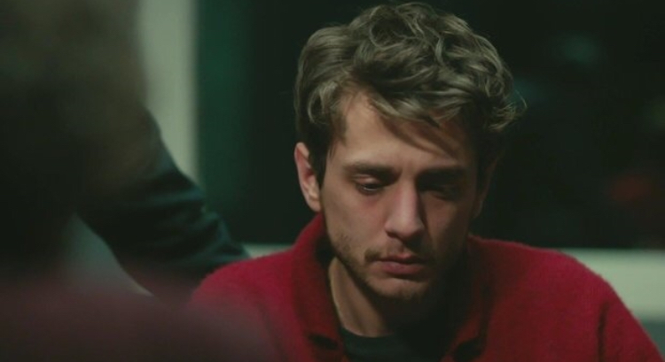 Masum Değiliz — A man in a red sweater looking down at a table.