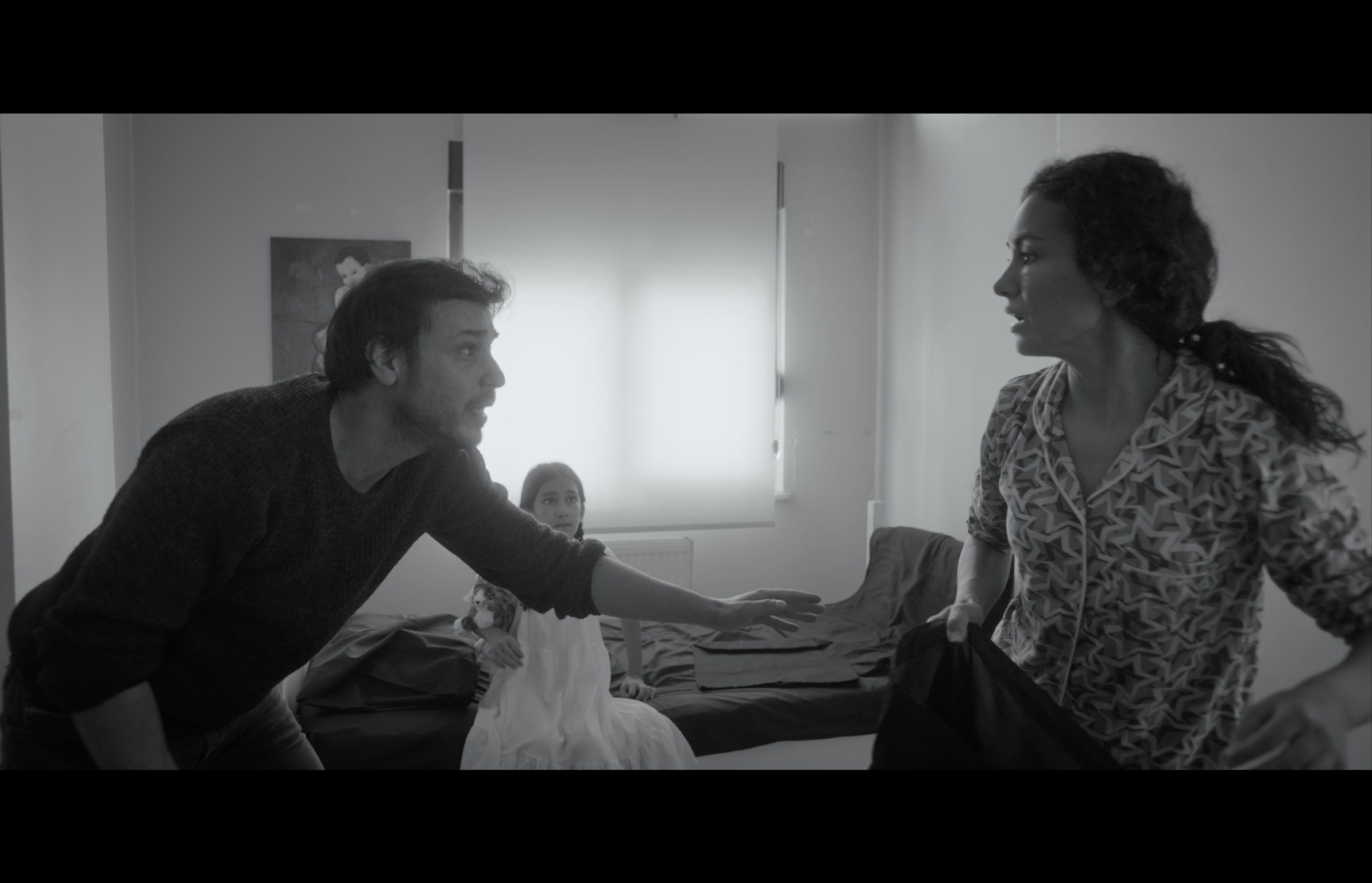 Sığınak — Black-and-white frame. A man reaching toward a woman with a girl seated behind them.